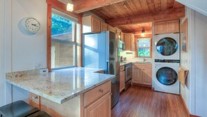A kitchen with wooden cabinets, a stainless steel refrigerator, a microwave, and a built-in washing machine. - Cozy cabin in the woods, minutes from town, beaches, hiking (Eastsound)