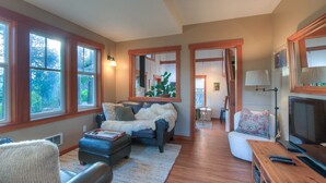 A spacious living room with a fireplace, large windows, and a cozy seating area. - Cozy cabin in the woods, minutes from town, beaches, hiking (Eastsound)
