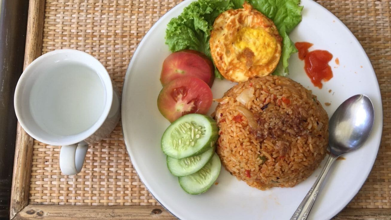 A plate with rice, a fried egg, lettuce, tomatoes, and cucumber slices, accompanied by a white mug and a spoon.
