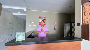 A reception desk with a person standing behind it, a fire extinguisher on the wall, and a sign indicating F&B service. - Ommaya Hotel & Resort (Baki)
