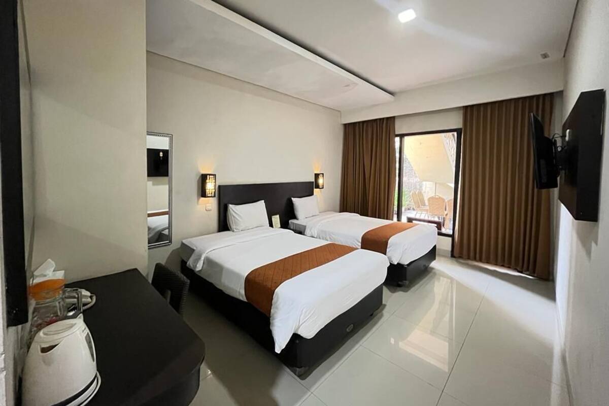 A hotel room with two beds, a desk with a coffee maker, and a TV mounted on the wall.