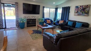 A living room with a sofa, a coffee table, a flat-screen TV, a fireplace, and a painting on the wall. - A tropical paradise in the desert! (Cathedral City)