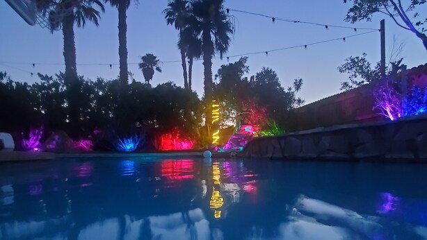 A swimming pool with colorful lights reflecting on the water, surrounded by palm trees and a clear sky. - A tropical paradise in the desert! (Cathedral City)