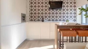 Une cuisine moderne avec un crédence à motifs, un four encastré et un coin repas comprenant une table en bois et des chaises en métal.