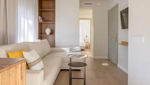 Un salon moderne comprenant un canapé, une petite table ronde, une bibliothèque et une porte donnant sur une autre pièce.