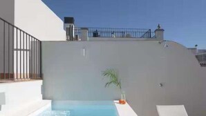 Une piscine sur le toit offrant une vue dégagée sur le ciel, une petite plante en pot et un fauteuil de relaxation blanc.