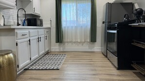 A modern kitchen with white cabinets, a stainless steel refrigerator, and a black stove. - Charming Guest House in East Sac (Sacramento)