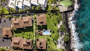 An aerial view of a coastal resort with multiple bungalow-style buildings, a swimming pool, and a rocky shoreline. - 🏖️Partial Ocean View Condo w/ A/C | Kona Isle B25 (Kailua Kona)