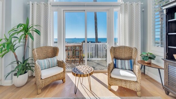 Een gezellige kamer met rieten stoelen, een ronde houten tafel en uitzicht op de oceaan door grote ramen.