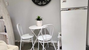 Una cocina compacta con un refrigerador blanco, un reloj de pared y una pequeña mesa de comedor con dos sillas.
