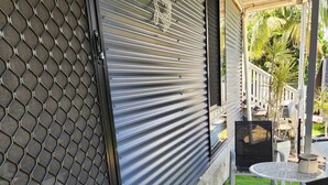 Un patio techado con una puerta de malla, una pequeña mesa con sillas y césped artificial.