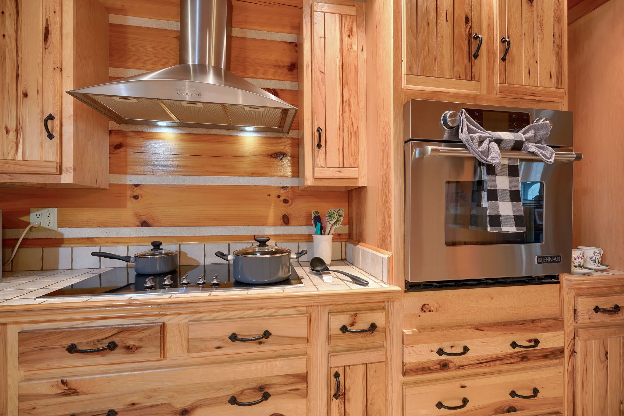 A kitchen with wooden cabinets, a stainless steel range hood, a Jenn-Air refrigerator, and a tiled backsplash.