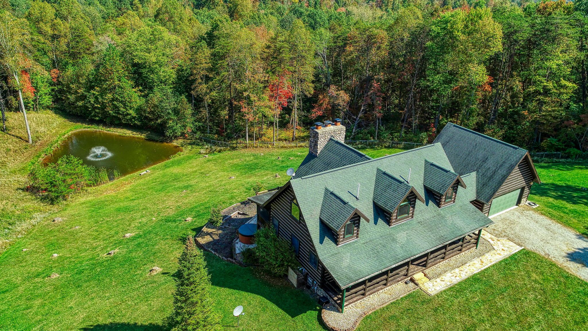 A log cabin with a stone chimney, surrounded by a well-maintained lawn and a pond.