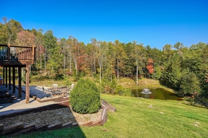 A wooden deck with outdoor furniture, a pond with a fountain, and a forested area. - Wow! Timber Ranch Lodge, 43 acres, Sleeps 12, Family and Pet Friendly!  (Logan)