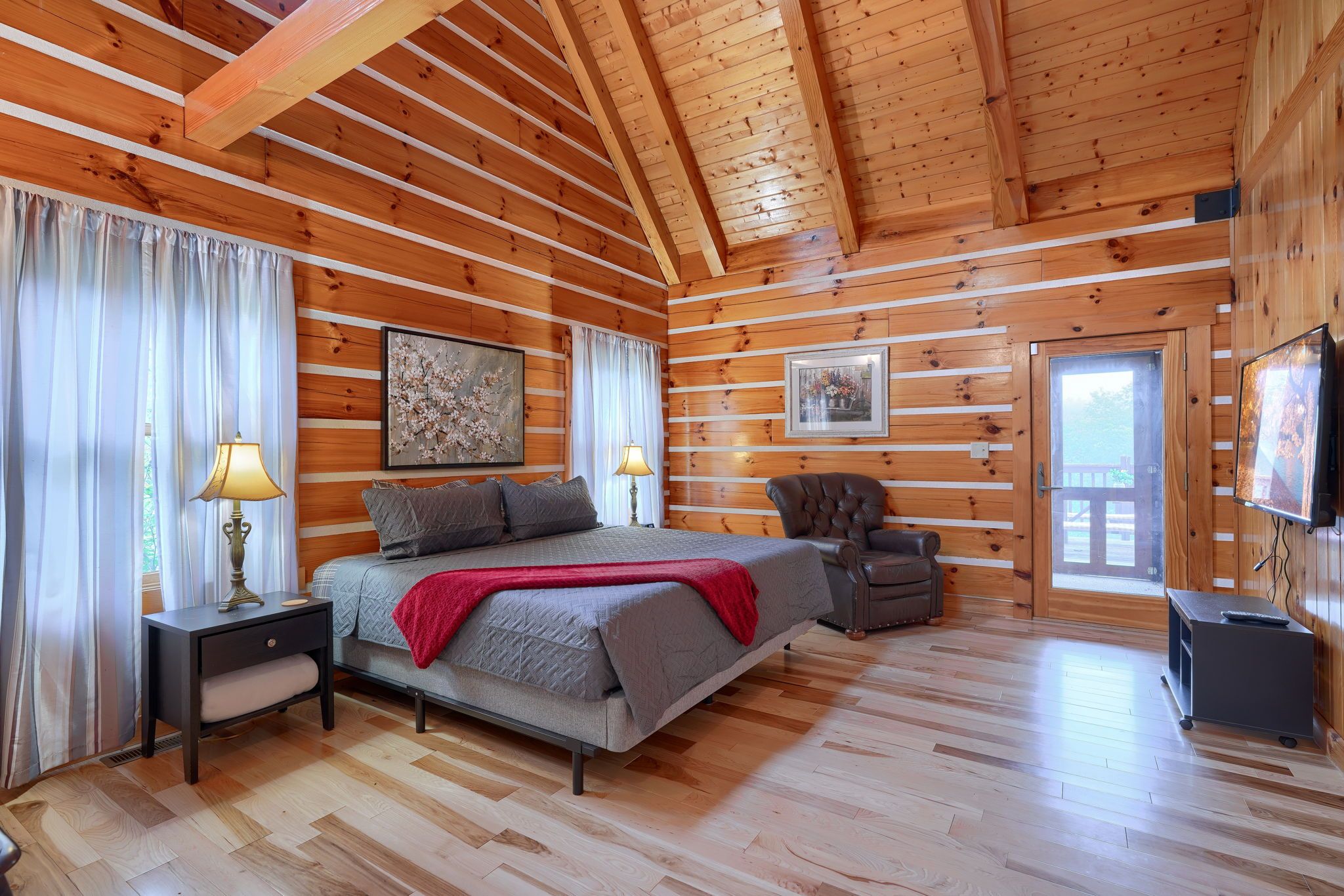 A log cabin bedroom with a bed, a chair, a TV, and a window.
