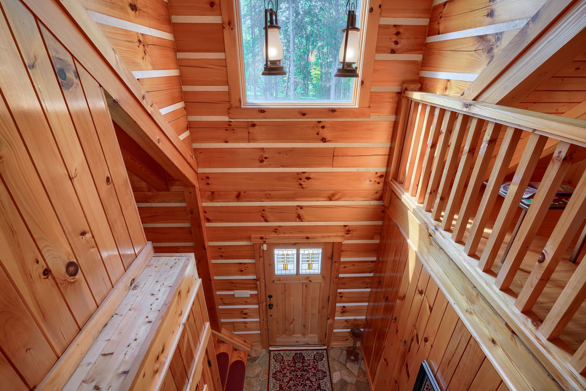 A wooden cabin interior with a central door, a small window, and a wooden staircase.