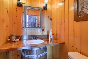 Un baño de madera con un lavabo de barril de madera, un espejo enmarco y una pequeña estatua.