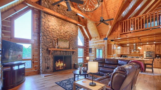 A spacious living area with a stone fireplace, leather sofa, and wooden flooring. - Wow! Timber Ranch Lodge, 43 acres, Sleeps 12, Family and Pet Friendly!  (Logan)