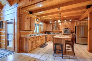 Interior de una cabaña de madera con cocina, que incluye armarios de madera, una isla central y un refrigerador de acero inoxidable.