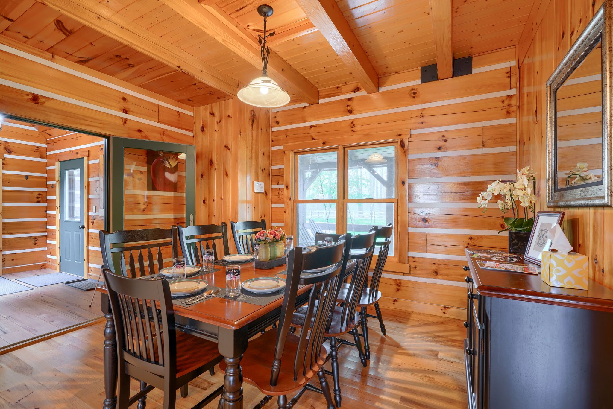 A wooden interior with a dining table set for four, surrounded by chairs, and a kitchen area with a stove and counter.