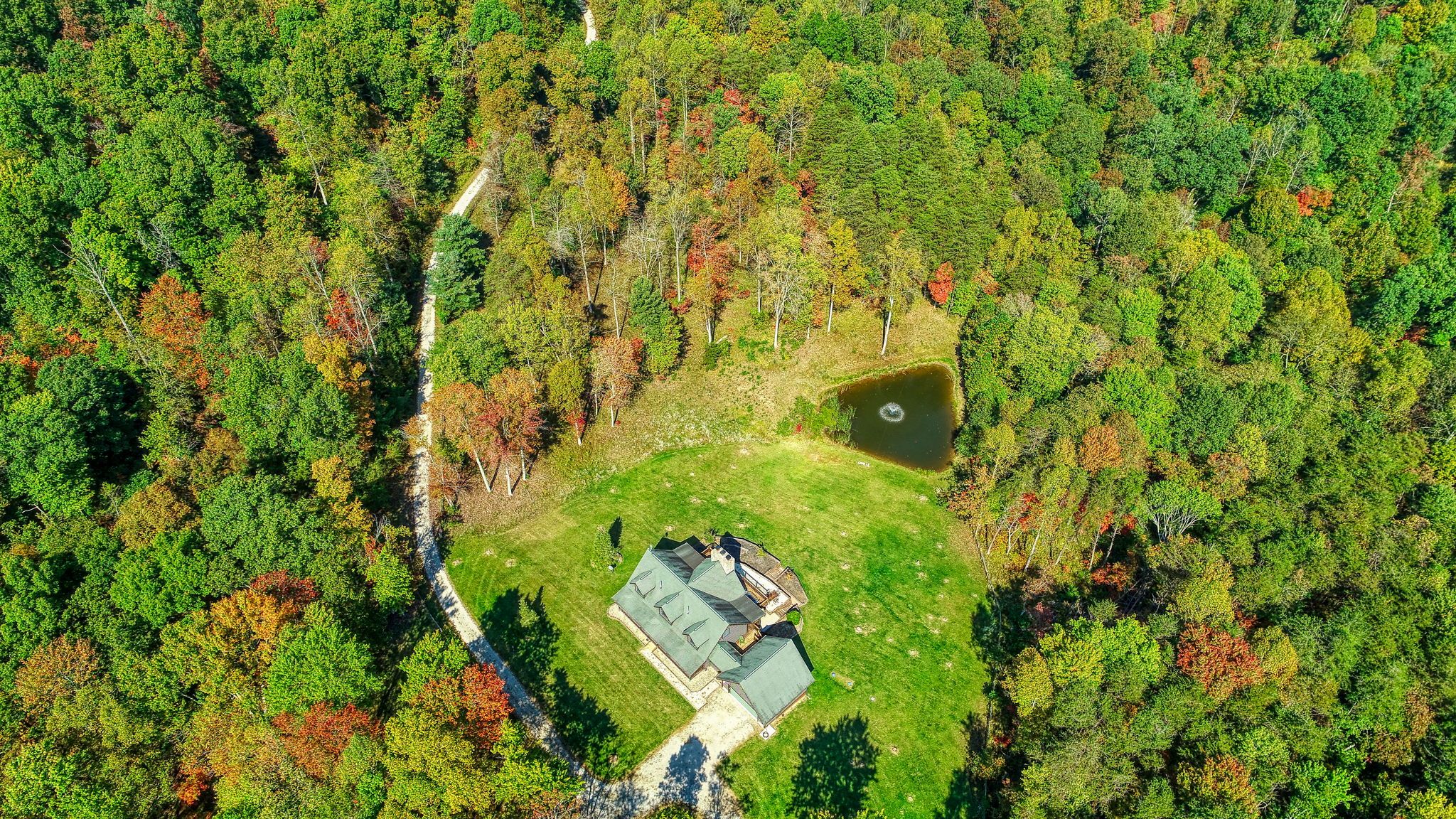 An aerial view of a property with a large lawn, a pond, and a building with a sloped roof.