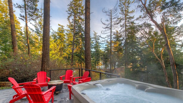 Et spabad omgivet af røde Adirondack-stole på en terrasse med skov i baggrunden.