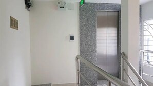 A staircase with a metal railing leading to an elevator. The walls are white with a grey speckled pattern. - New Paris Hotel - by Bay Luxury (Ho Chi Minh City)