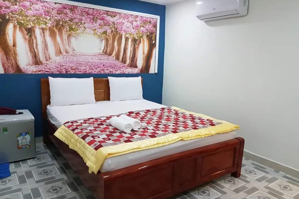 Un dormitorio con cama, una mesita de noche, aire acondicionado instalado en la pared y un cuadro de flores grande sobre la cama.