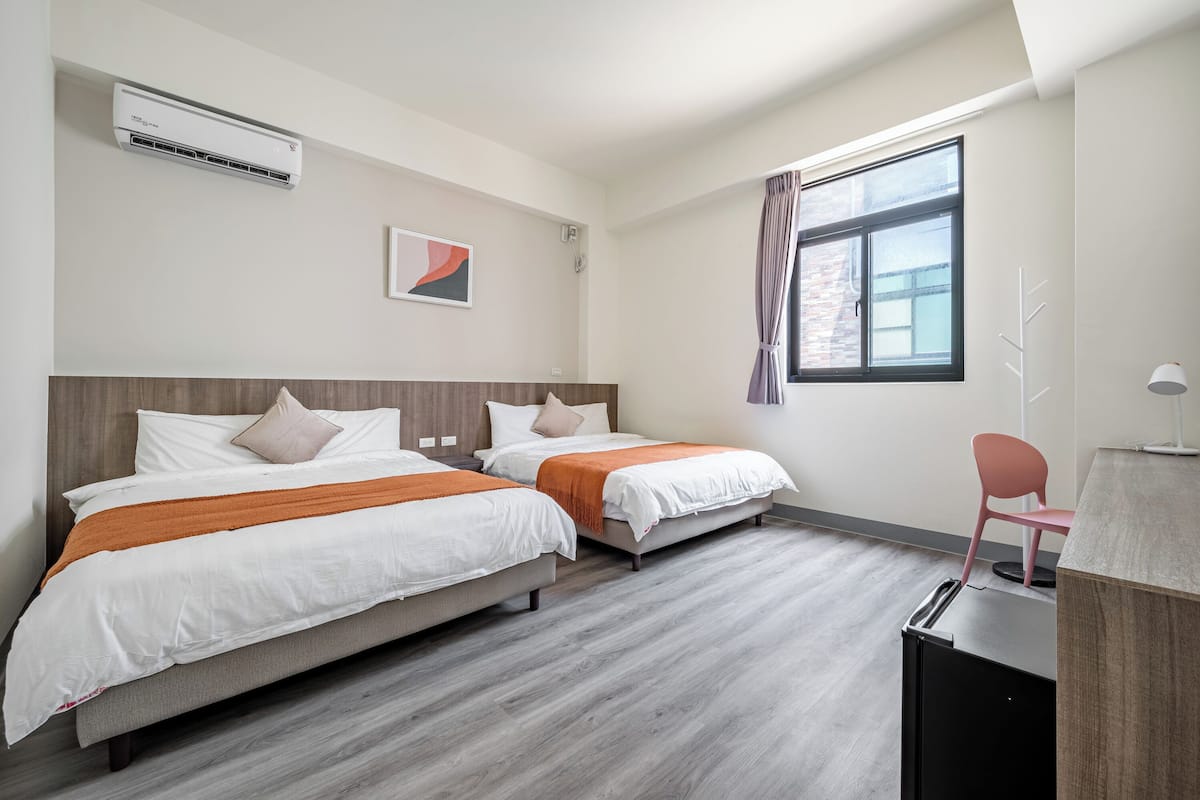 A hotel room with two beds, a desk, a chair, and a window with curtains.