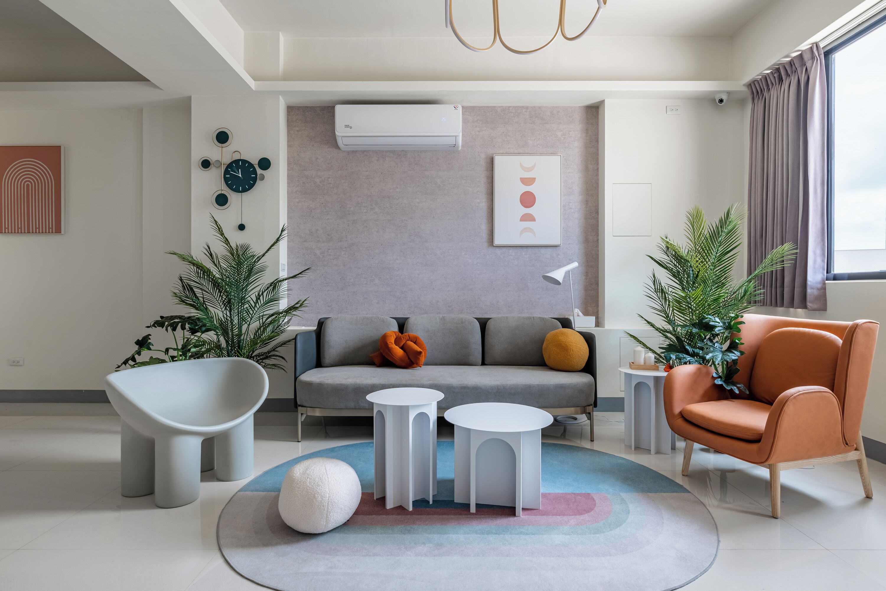 A modern living room with a grey sofa, white side tables, a white chair, and decorative plants.