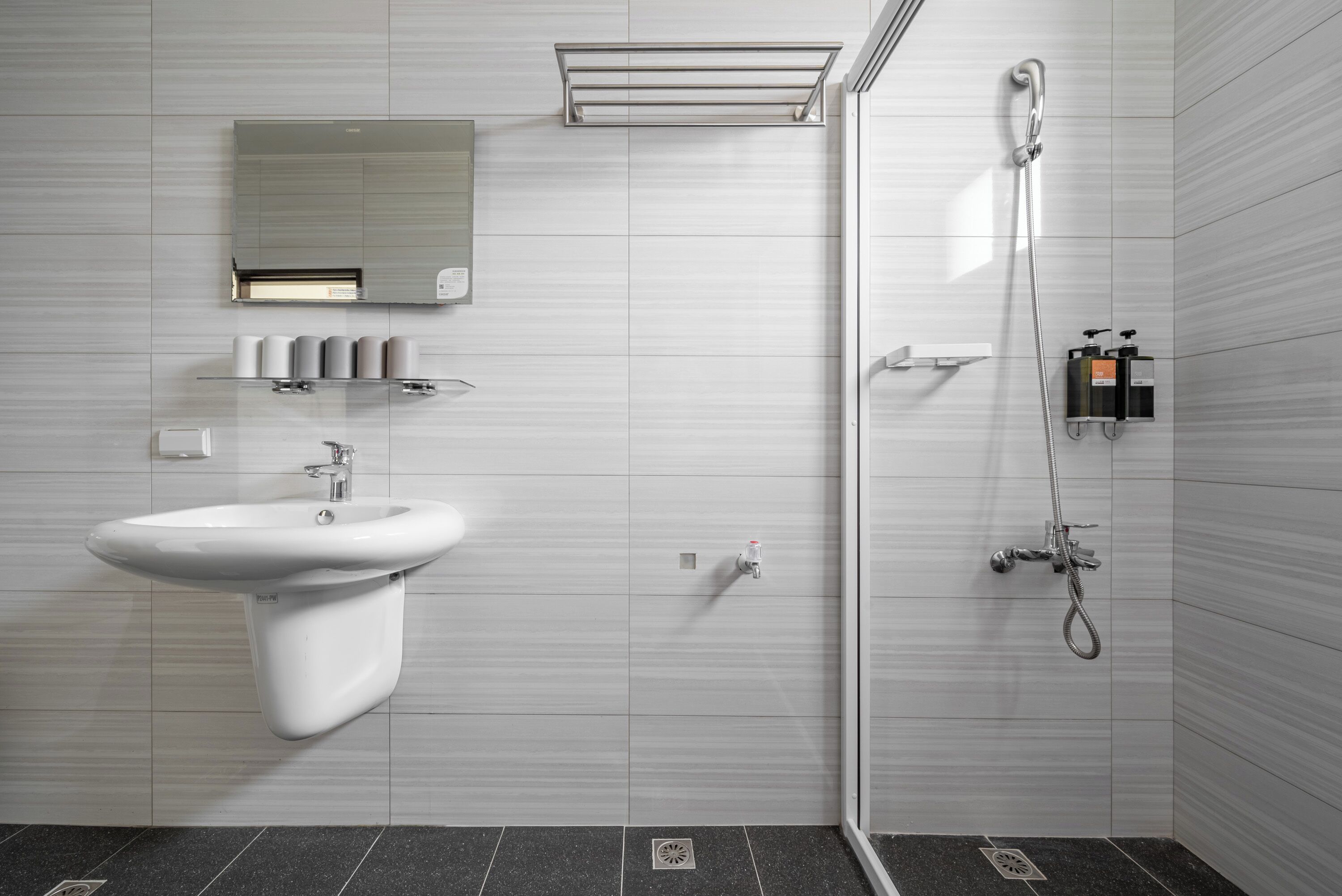 A modern bathroom with a white sink, a mirror, a shower, and a towel rack.