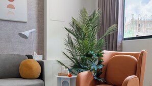 A modern living room with a grey sofa, an orange armchair, a round coffee table, and a large potted plant. - Penghu Lemongrass Easy Stay (Magong)