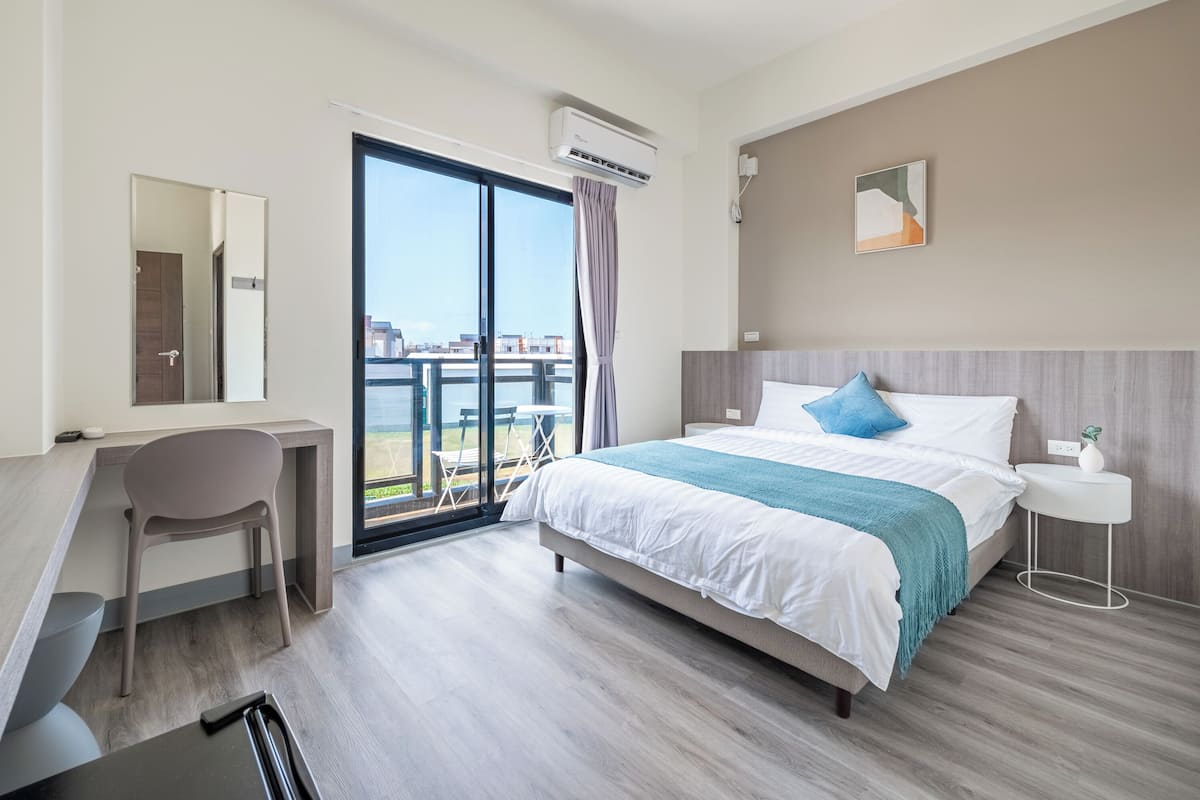 A modern hotel room with a bed, desk, chair, and a large window with a view.