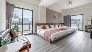 A modern hotel room with a large bed, a sofa, a dining table, and a view of the city through large windows. - Penghu Lemongrass Easy Stay (Magong)