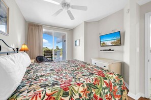 Un dormitorio con cama, ventilador de techo, televisor y vistas al exterior.