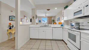 A modern kitchen with white cabinetry, a built-in oven, microwave, and dishwasher. There is a small island with a sink and a vase of flowers.