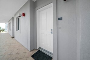 En bygning med facade, hvide dør, et overvågningskamera og et skilt med en kode.
