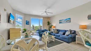 A living room with a blue sofa, white wicker chairs, a glass coffee table, and a ceiling fan.