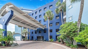 A modern building with a blue facade, a covered entrance, and palm trees.