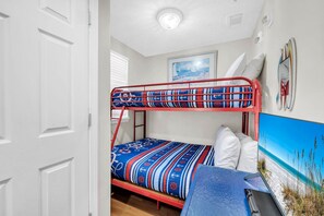 A bunk bed with a nautical-themed bedding, a desk with a laptop, and a beach-themed painting on the wall.