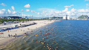 Une plage où l’on voit des gens se baigner et bronzer, une jetée et un phare en arrière-plan.