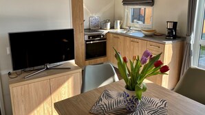 A compact kitchen with a built-in oven, a microwave, and a sink. There is a dining table with a vase of flowers and a patterned placemat. - Tiny Haus Waldsee Lodge by Interhome (Wemding)