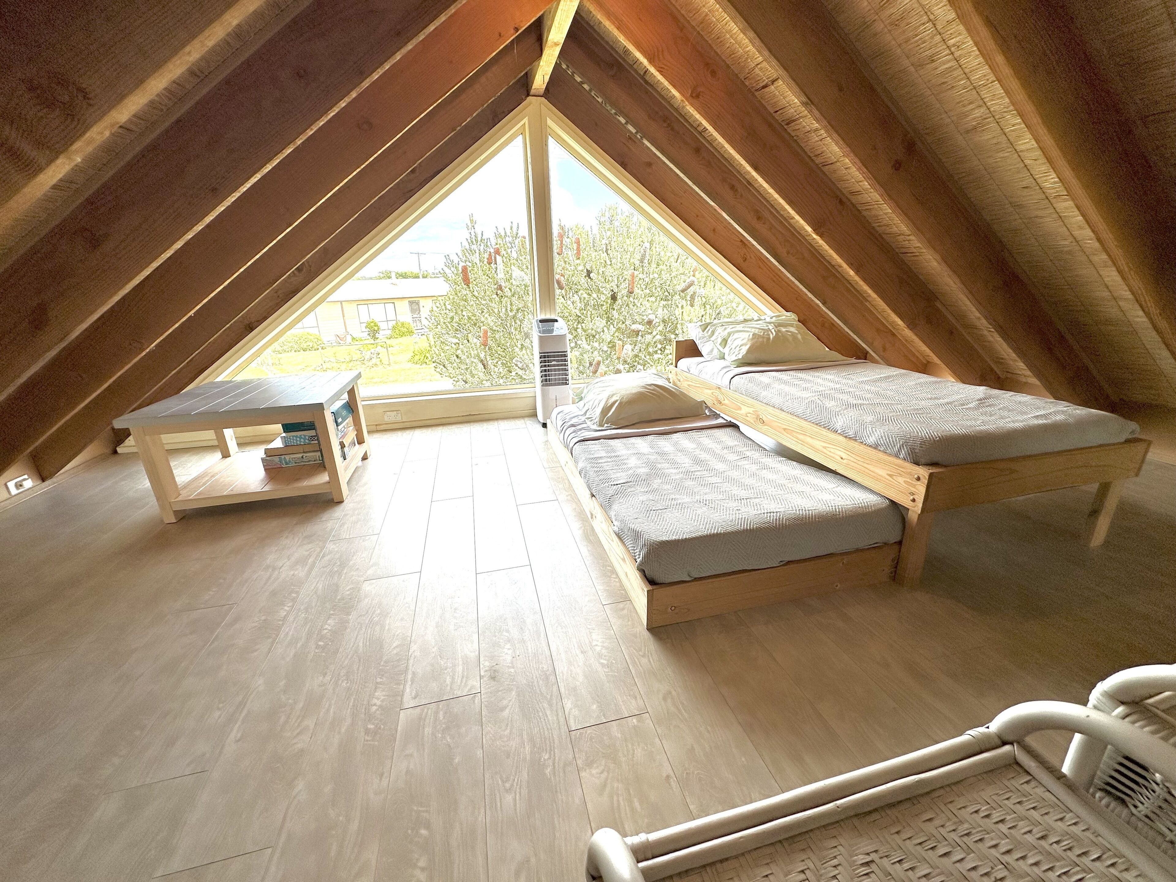 A small attic bedroom with two beds, a table, and a window.