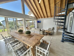 Un amplio salón con una gran mesa de madera, sillas blancas, un sofá y una escalera.