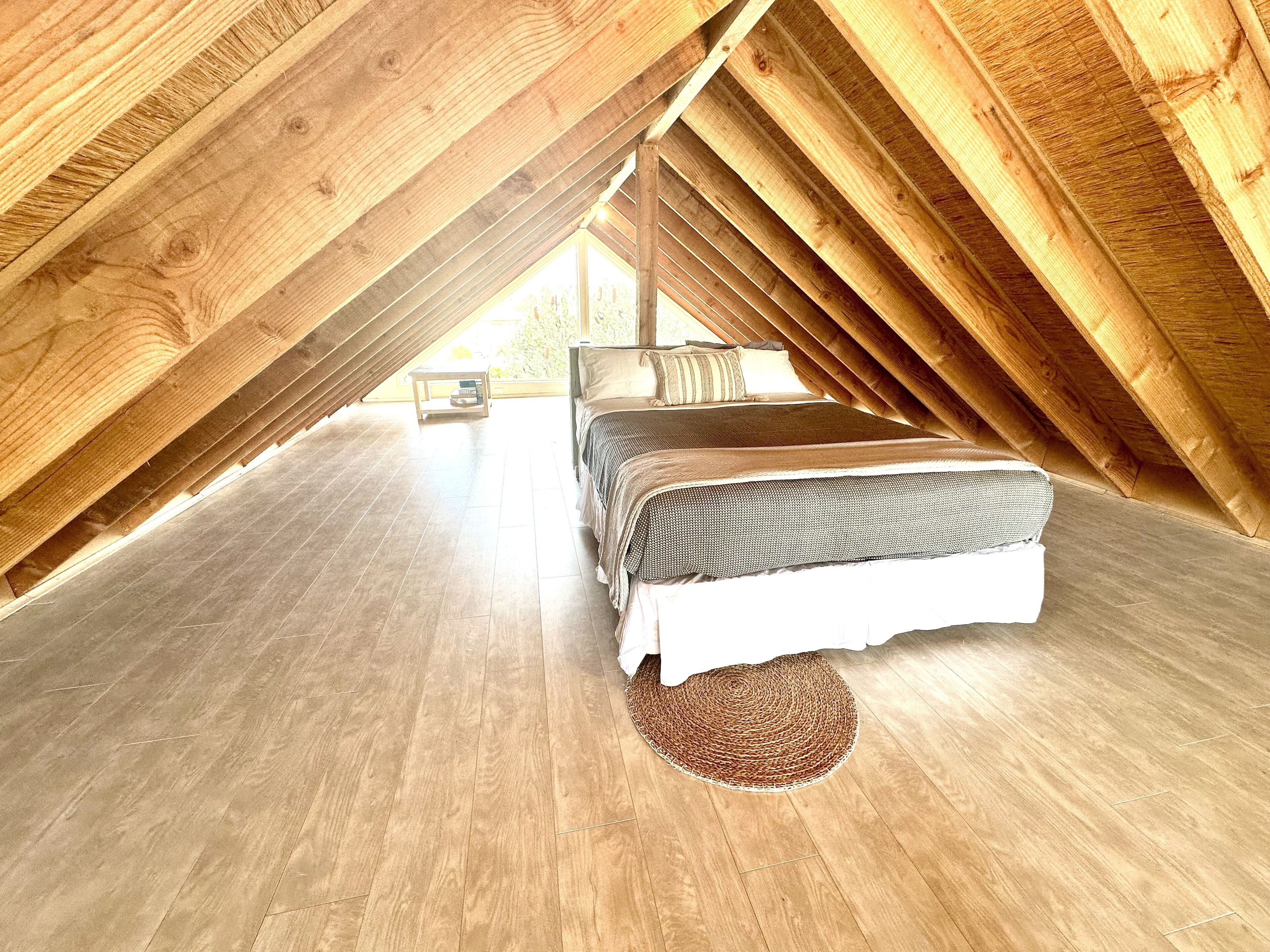 Une chambre aménagée sous les toits, avec un lit, une petite table et une vue à travers le plafond en pente.