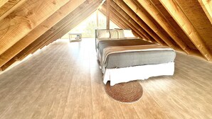 An attic bedroom with a bed, a small table, and a view through the sloped ceiling. - Betty on Bayview - Surf Beach  (Surf Beach)