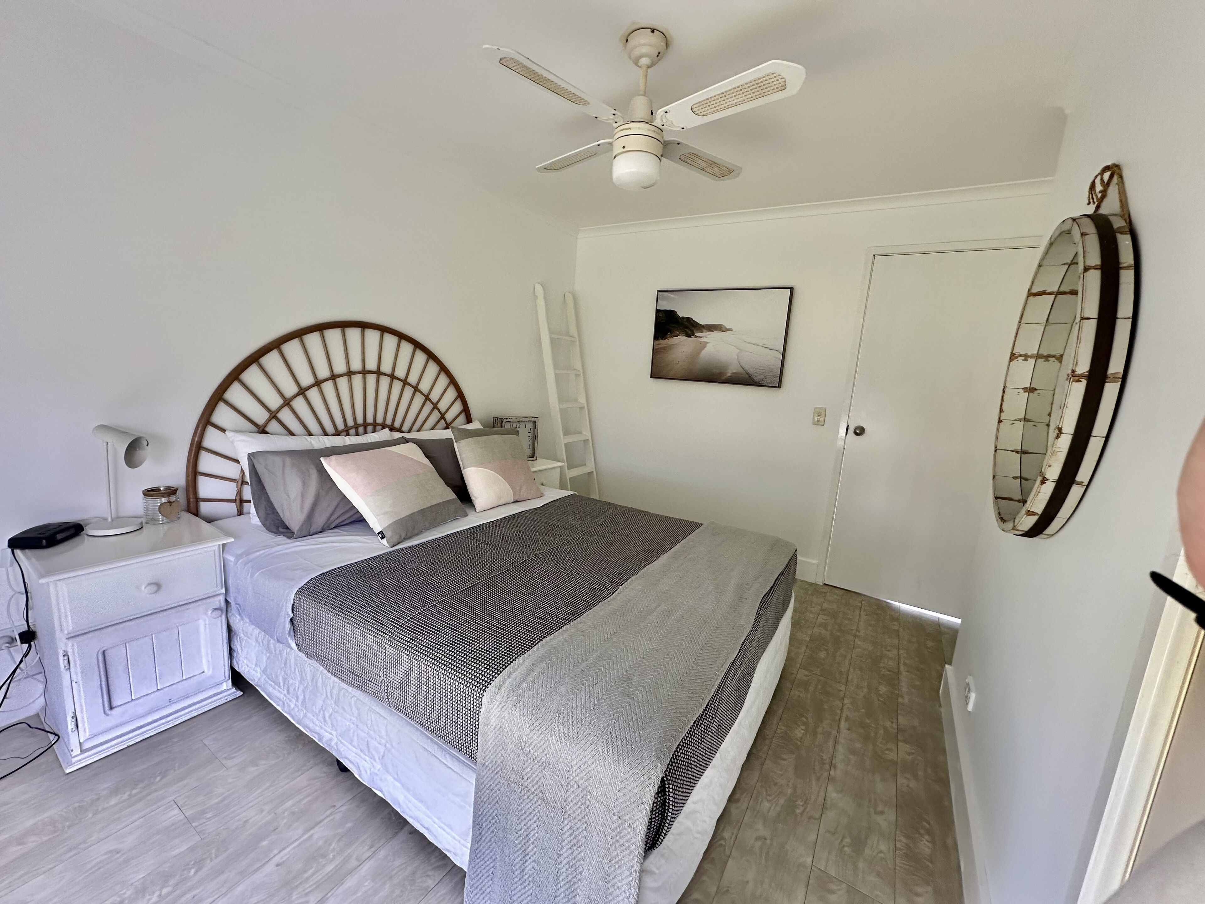 Ein Schlafzimmer mit Bett, Nachttisch, Nachttischlampe, Deckenventilator und einem an der Wand hängenden Bild.