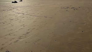 A wide sandy beach with footprints and rocks, a clear sky, and a distant hill. - Betty on Bayview - Surf Beach  (Surf Beach)