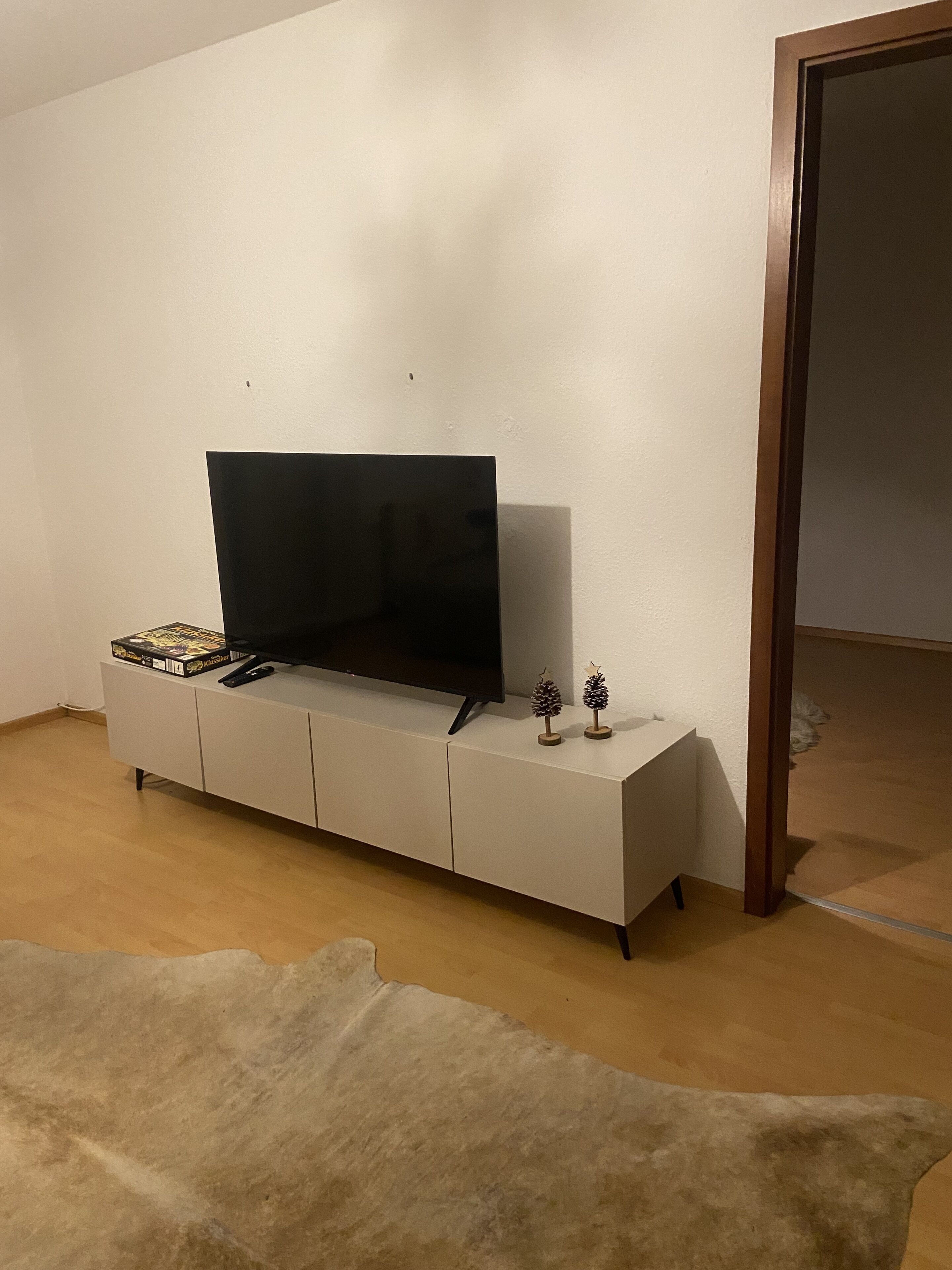 Una habitación con un armario blanco, un televisor encima y una puerta a la derecha.
