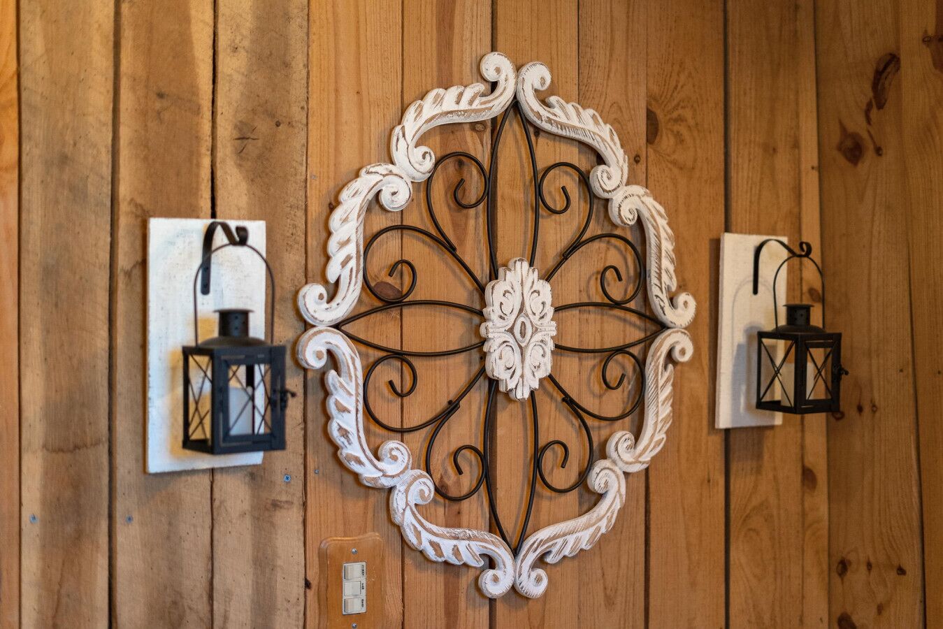 A wall with a decorative metal piece and two wall-mounted lanterns.